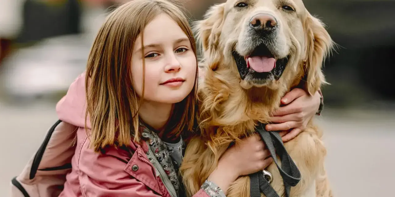 Dziewczynka w różowej kurtce przytula uśmiechniętego golden retrievera.